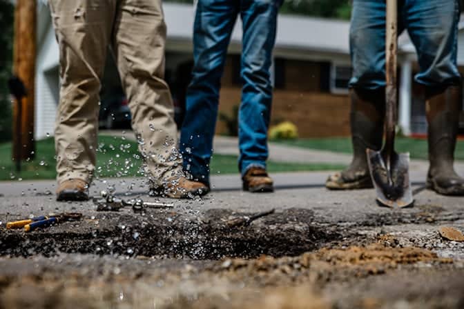 Three utility workers with tools observing a service line leak